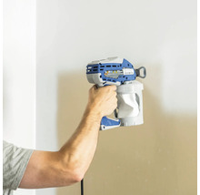 Eine Person hält eine Farbspritzpistole vor eine Wand