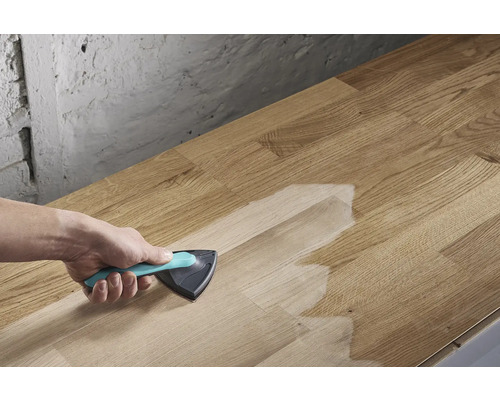 Eine Person trägt Oberflächenbehandlung mit einem Dreieckspinsel auf eine Holzplatte auf.