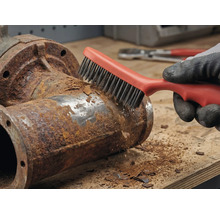 Eine Person entfernt mit einer Drahtbürste Rost von einem Metallrohr.