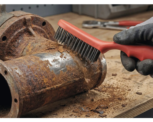 Eine Person entfernt mit einer Drahtbürste Rost von einem Metallrohr.