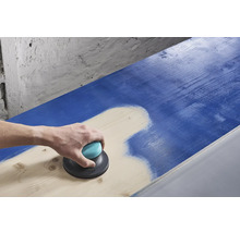 Eine Person schleift mit einem Exzenterschleifer eine blaue Holzoberfläche ab.