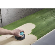 Eine Person schleift mit einem Exzenterschleifer eine grün gestrichene Holzoberfläche ab.