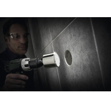 Mann bohrt mit einer Diamantbohrkrone ein Loch in eine Fliese.