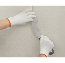 Hände mit Handschuhen bearbeiten eine Tapete mit einem Multifunktionswerkzeug