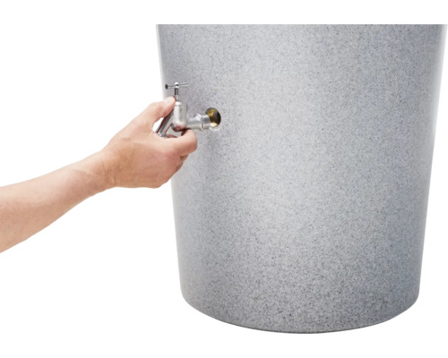 Eine Hand schraubt einen Auslaufhahn aus Metall in einen grauen Regenspeicher in Granitoptik.