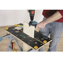 Eine Person bohrt ein Holzbrett mit einer Bohrmaschine auf einer Werkbank.