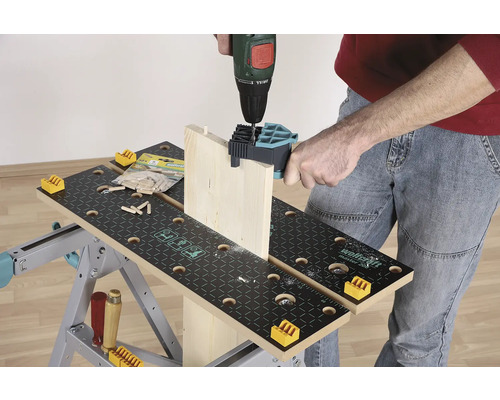 Eine Person bohrt ein Holzbrett mit einer Bohrmaschine auf einer Werkbank.