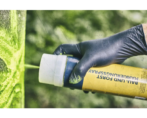 Eine Person mit Handschuhen verwendet Markierungsspray für Bau und Forst.