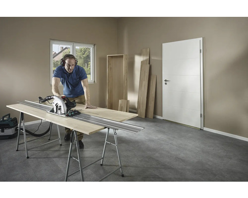 Mann schneidet Holz mit einer Handkreissäge auf einer Werkbank in einem Raum.