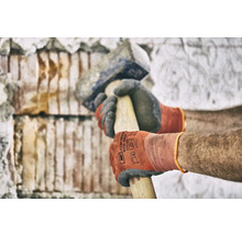 Mann mit Handschuhen bearbeitet Mauerwerk mit einem Fäustel