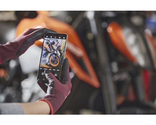 Ein Smartphone in behandschuhten Händen fotografiert ein Motorrad.