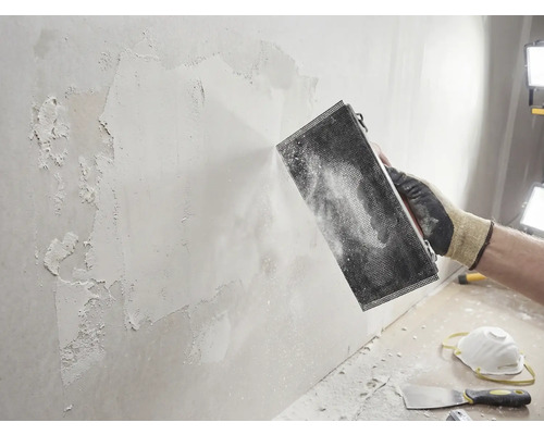 Handwerker schleift Wand mit Schleifwerkzeug. Heimwerkerprojekt zur Wandrenovierung.