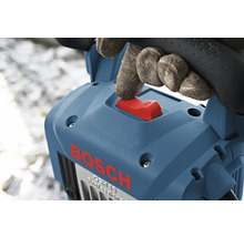 Hand mit Handschuh betätigt den roten Schalter eines blauen Bosch Stemmhammers.