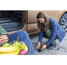 Frau bedient eine elektrische Luftpumpe neben einem Fahrzeug