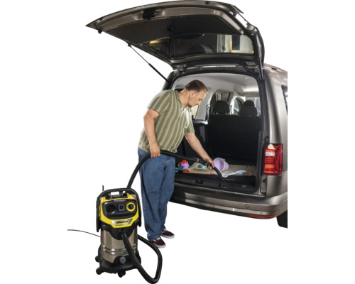 Mann saugt mit einem Mehrzwecksauger den Kofferraum eines Autos aus. Kärcher Logo sichtbar.