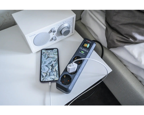 Steckdosenleiste mit Überspannungsschutz und angeschlossenem Telefon auf einem Nachttisch