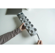 Eine Person hält eine graue Steckdosenleiste mit zehn Steckplätzen.