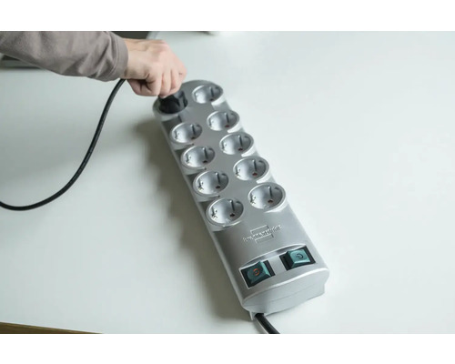 Person steckt Stecker in eine graue Steckdosenleiste mit zehn Steckplätzen