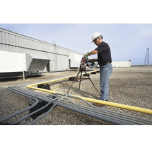 Ein Mann in Arbeitskleidung schneidet auf einem Dach Rohre mit einer Rohrsäge.