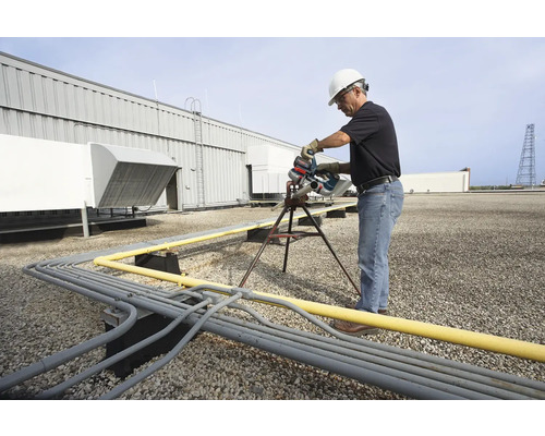 Ein Mann in Arbeitskleidung schneidet auf einem Dach Rohre mit einer Rohrsäge.