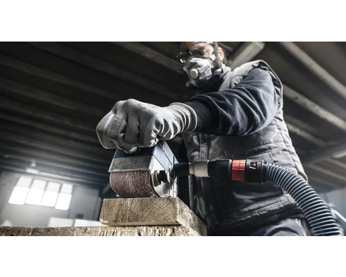 Ein Mann schleift mit einer Schleifmaschine ein Stück Holz. Er trägt eine Schutzmaske und Schutzbrille.