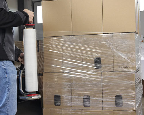 Eine Person wickelt Kartons mit einer Stretchfolienverpackung ein.