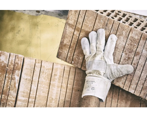 Ein Arbeiter trägt mit Handschuhen Ziegelsteine.