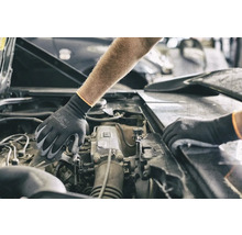 Eine Person mit Schutzhandschuhen arbeitet an einem Automotor.