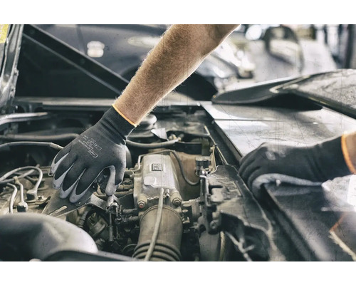 Eine Person mit Schutzhandschuhen arbeitet an einem Automotor.