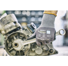 Hand mit Arbeitshandschuh und Schraubenschlüssel an einem Motor