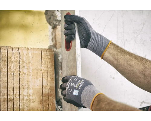 Mann mit Arbeitshandschuhen und Wasserwaage bei Renovierungsarbeiten.