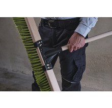 Person hält eine grüne Kehrbürste mit Holzstiel.