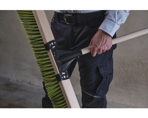 Person hält eine grüne Kehrbürste mit Holzstiel.