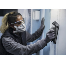 Eine Person trägt Schutzkleidung und glättet eine Wand mit einem Glättwerkzeug.