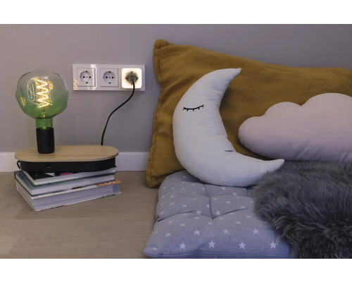 Dekorative LED-Filamentlampe auf einem Bücherstapel in einem Kinderzimmer mit Mondkissen, Wolkenkissen und einer Dreifachsteckdose an der Wand.