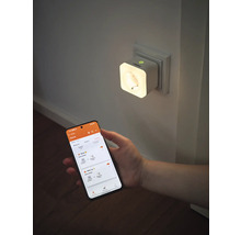 Smarte OSRAM Steckdose mit integriertem Nachtlicht in einer Wandsteckdose, gesteuert über eine App auf einem Smartphone.