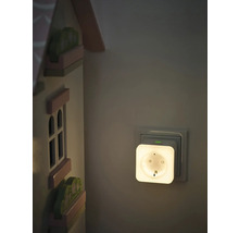 OSRAM Smart Plus Plug Nachtlicht in einer Wandsteckdose neben einem hölzernen Spielzeughaus in einem sanft beleuchteten Raum.