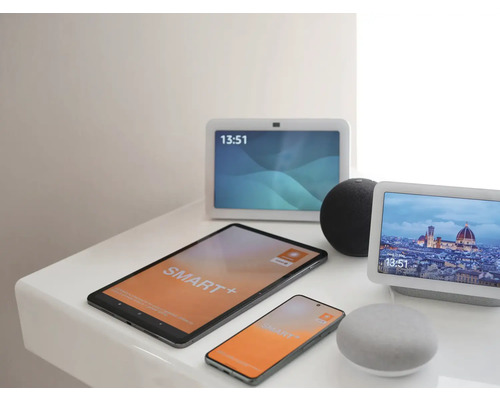 Verschiedene Smart Home Geräte wie Tablet, Smartphone, Smart Displays und Lautsprecher zur Steuerung auf einer hellen Ablagefläche.