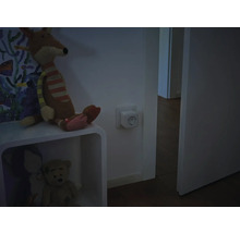 Smarte Steckdose in einer Wandsteckdose in einem gedimmten Raum neben einem Regal mit Stofftieren.