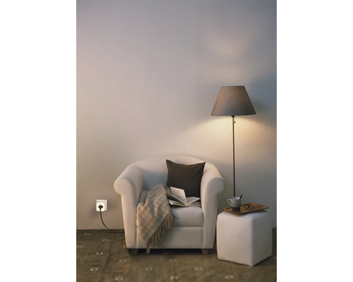 Gemütliche Leseecke mit Sessel, Stehleuchte, Hocker und einer smarten Steckdose in der Wand.