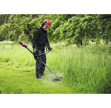 Mann mit Helm und Gehörschutz mäht Gras mit einem Rasentrimmer.