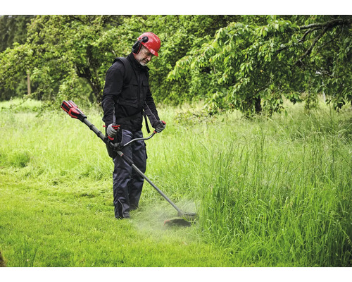 Mann mit Helm und Gehörschutz mäht Gras mit einem Rasentrimmer.