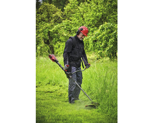 Eine Person benutzt einen Rasentrimmer in einem Garten, geschützt mit einem Helm und Gehörschutz.