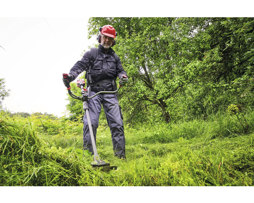 Mann mit Schutzhelm und Gehörschutz beim Rasentrimmen im Garten