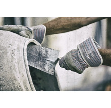 Nahaufnahme einer Person, die beim Betonmischen Schutzhandschuhe und eine Maurerkelle verwendet