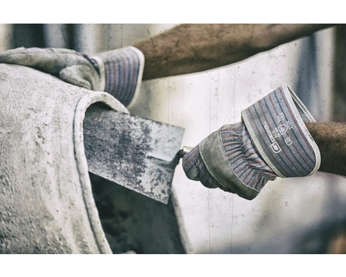 Nahaufnahme einer Person, die beim Betonmischen Schutzhandschuhe und eine Maurerkelle verwendet