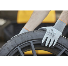 Eine Person mit Schutzhandschuhen hält einen schwarzen Reifen.