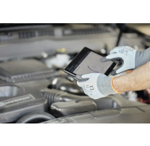 Ein Mechaniker mit Schutzhandschuhen verwendet ein Tablet am Motor eines Autos.