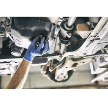 Eine Hand mit Arbeitshandschuh wechselt das Öl an einem Auto.