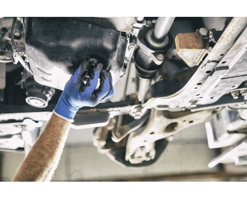 Eine Hand mit Arbeitshandschuh wechselt das Öl an einem Auto.